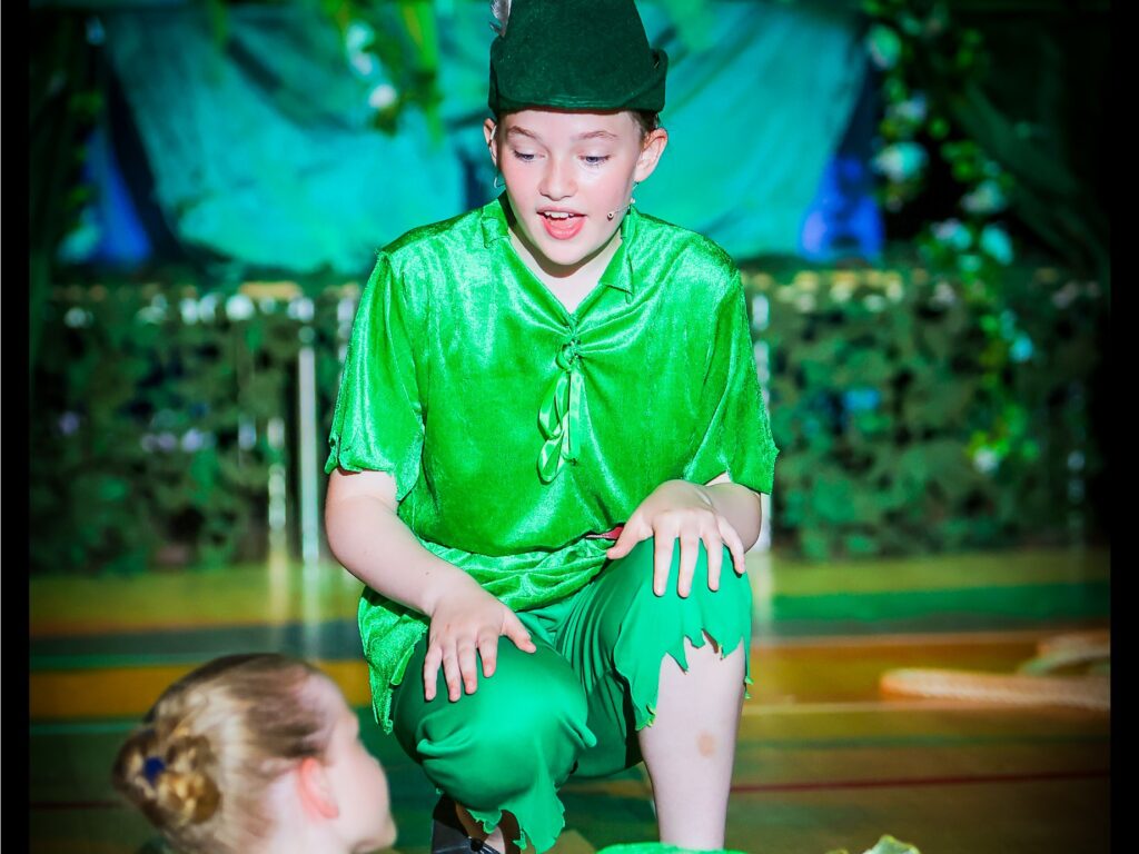 Child in a bright green costume on stage, wearing a green hat with a feather, mid-performance.
