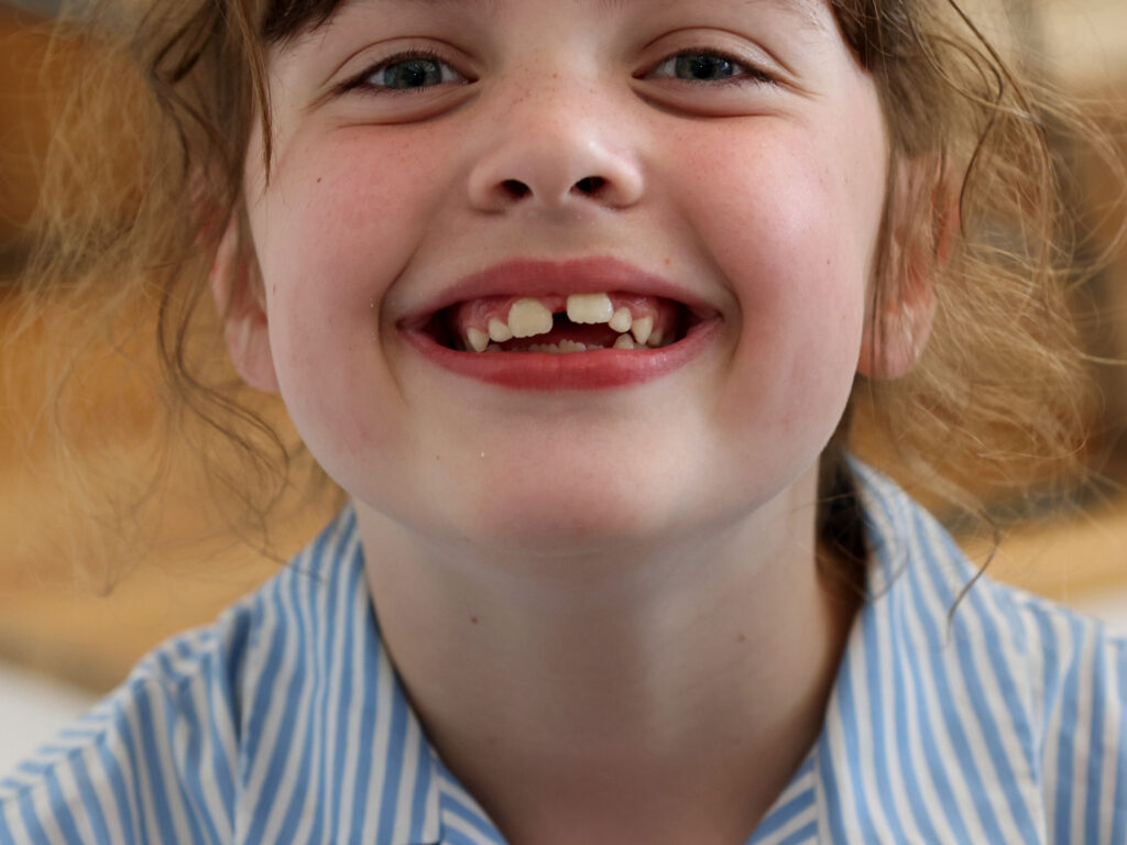 Close-up of a smiling girl with light brown hair and blue striped shirt.