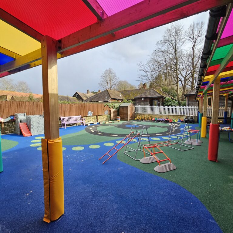 Colorful outdoor playground under a wooden shelter with rainbow translucent panels and blue/green rubber flooring.